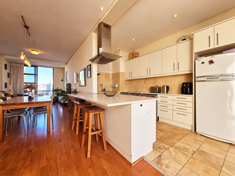 Open-plan living and kitchen area featuring a central island, modern cabinetry, tiled kitchen flooring, and laminate flooring in the dining space with balcony access.