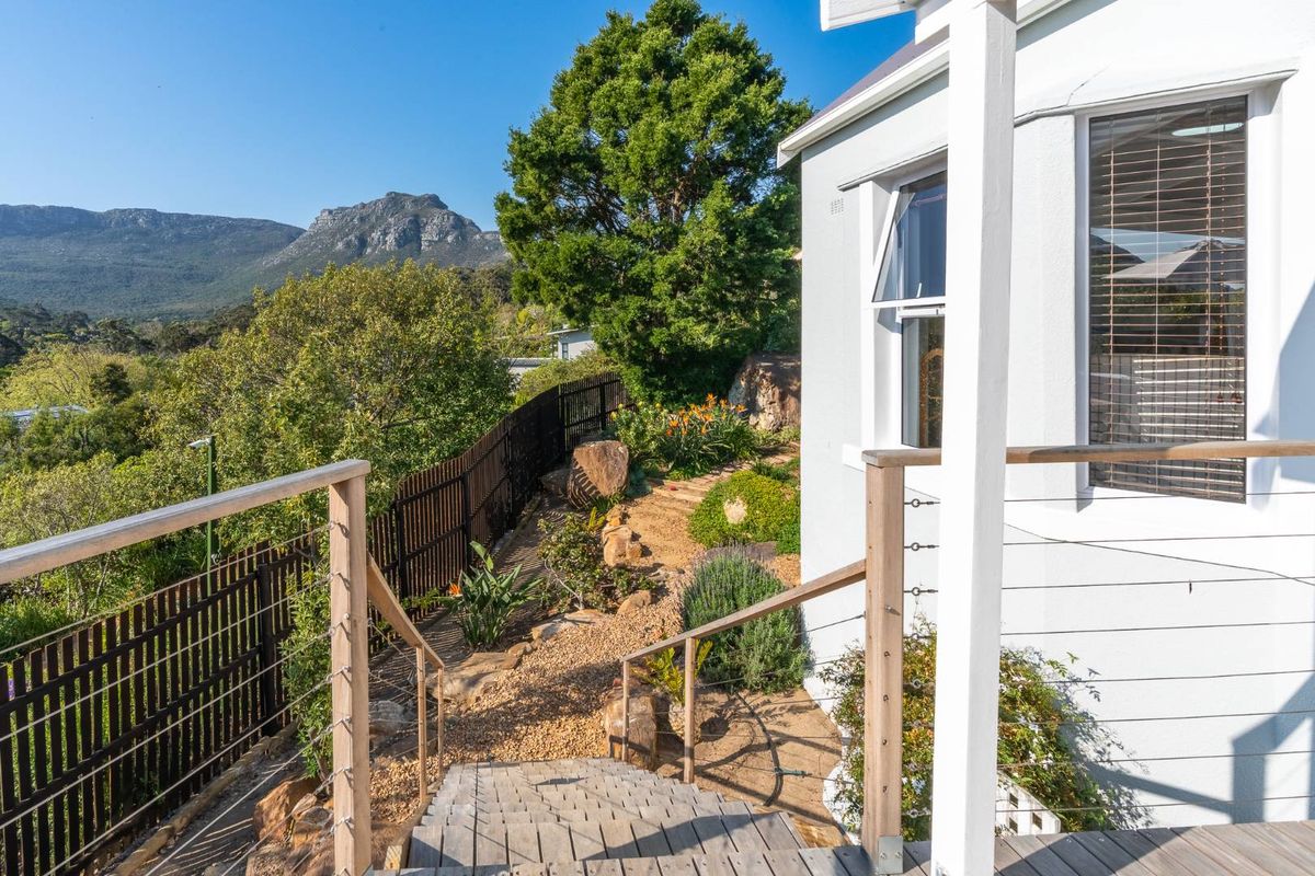 A well-maintained rear garden area featuring timber decking, cable railings, and a gravel pathway leading through landscaped grounds with mountain views.