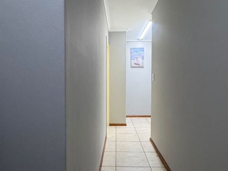 A clean and functional hallway featuring neutral wall paint, tiled flooring, and simple coving details.