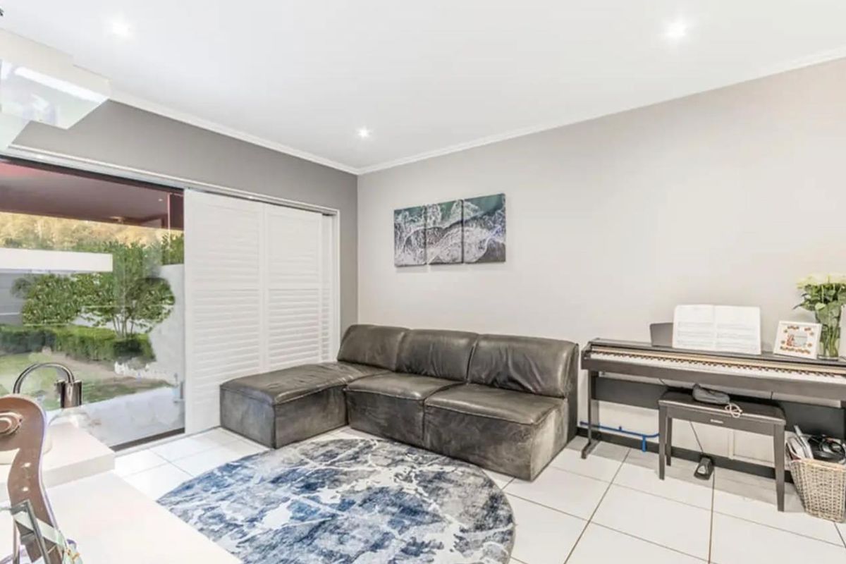 Bright living room featuring tiled flooring, recessed downlights, and a large sliding glass door with white plantation shutters providing access to the outdoor area.