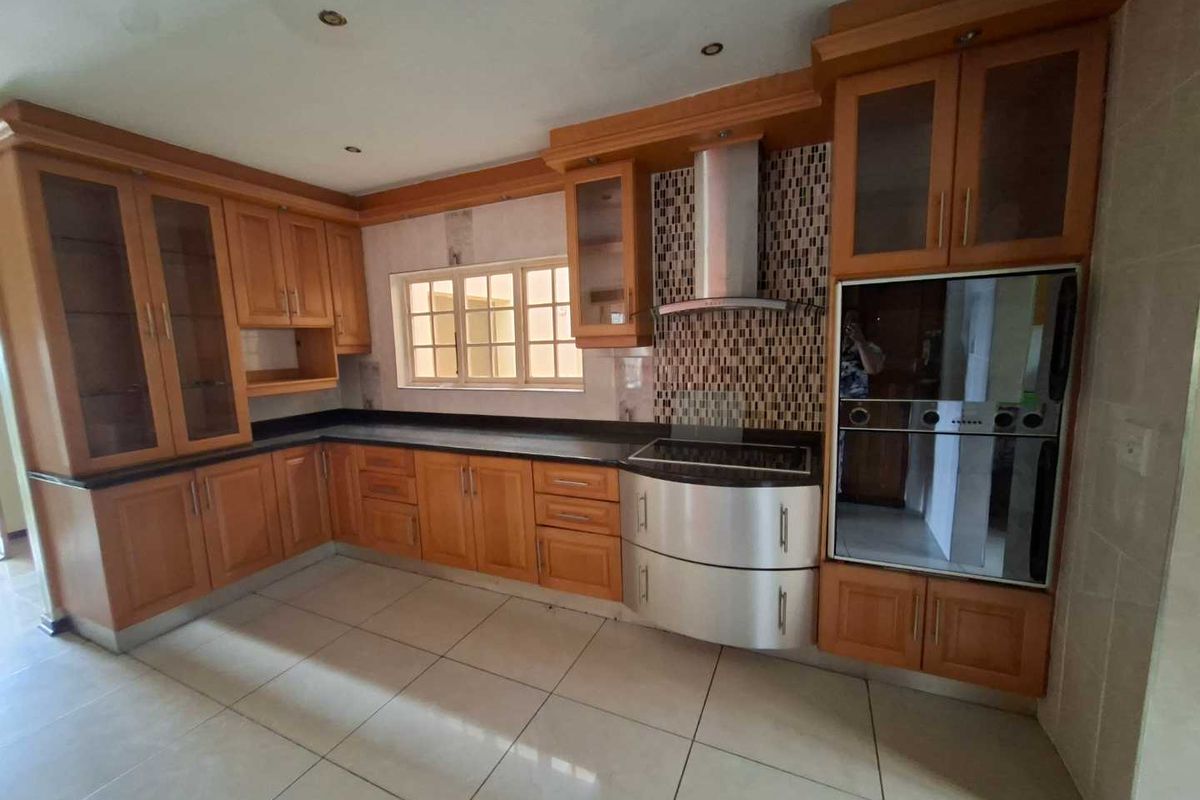 A functional kitchen featuring wooden cabinetry, granite countertops, a built-in oven, and a stainless steel extractor fan with mosaic tile backsplash.