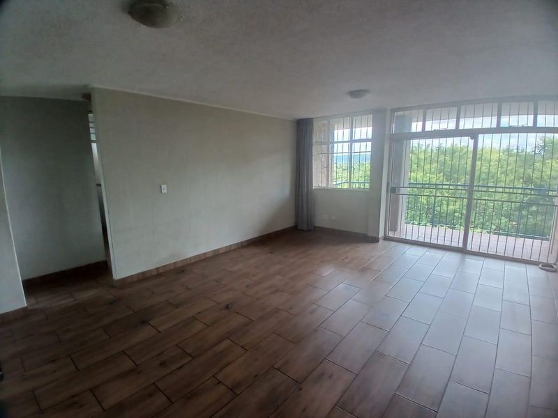 Spacious, empty living area featuring wood-look tile flooring and large sliding glass doors leading to a balcony with security bars.