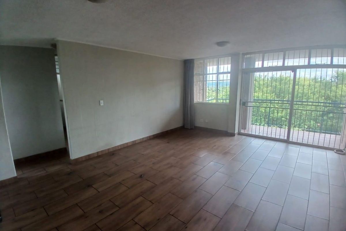 Spacious, empty living area featuring wood-look tile flooring and large sliding glass doors leading to a balcony with security bars.