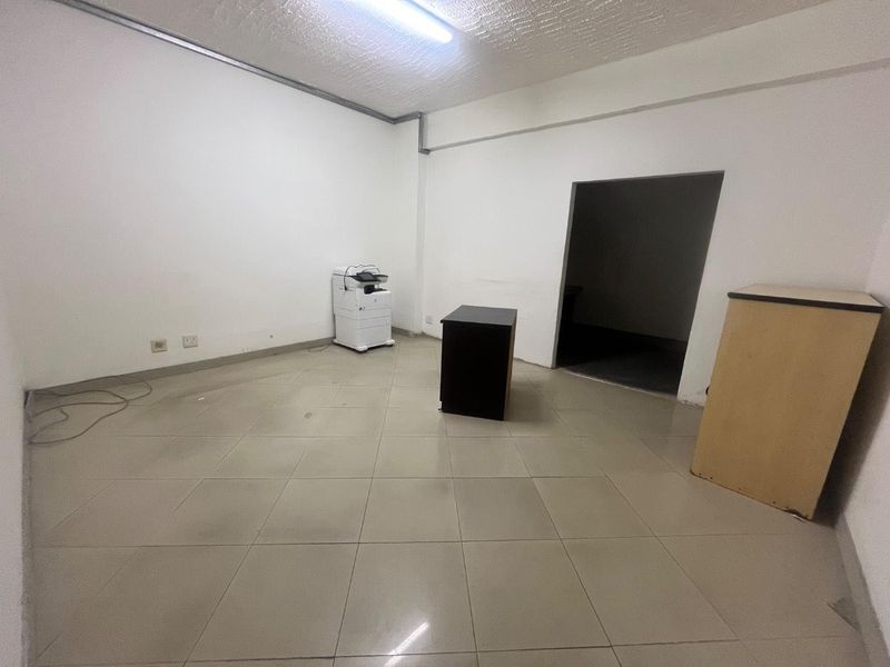 A vacant office space featuring tiled flooring, white walls, and overhead fluorescent lighting, suitable for a professional workspace or commercial use.