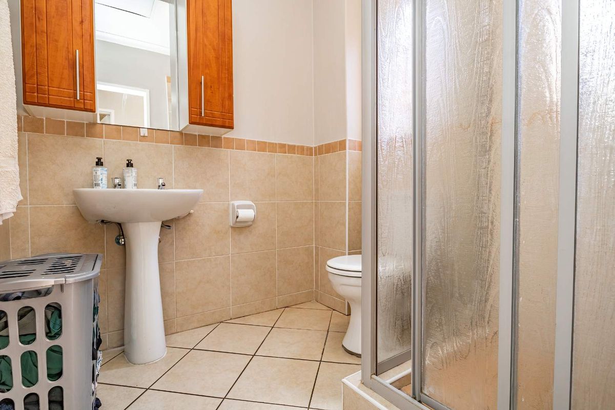 A functional bathroom featuring a pedestal sink, a shower enclosure with textured glass, a toilet, and neutral wall and floor tiling.