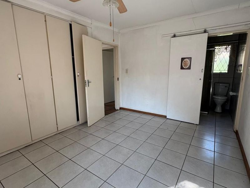 An empty bedroom featuring tiled flooring, built-in cupboards, a ceiling fan, and direct access to an en-suite bathroom.