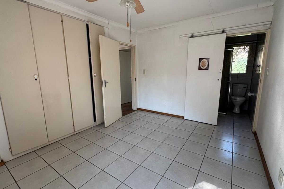 An empty bedroom featuring tiled flooring, built-in cupboards, a ceiling fan, and direct access to an en-suite bathroom.