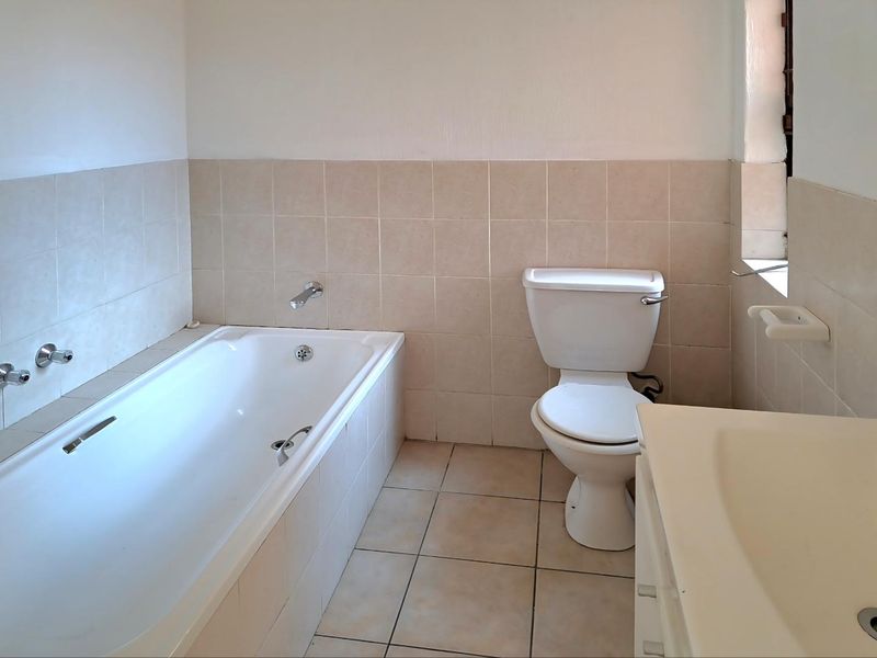 A functional bathroom featuring a built-in bathtub, standard toilet, and vanity basin with neutral wall and floor tiling.