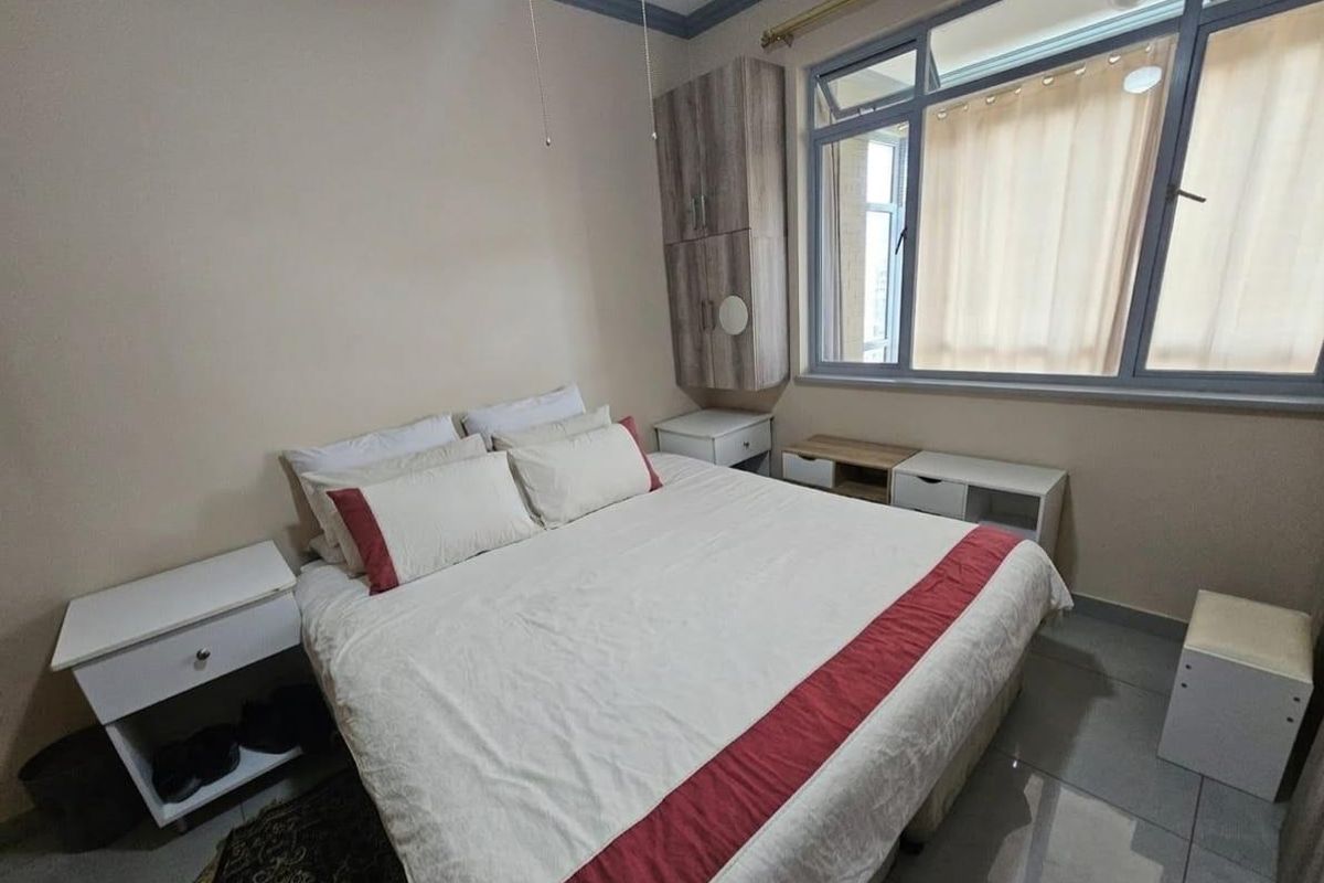 A functional bedroom featuring tiled flooring, built-in wall cabinetry, and large windows allowing for natural light.