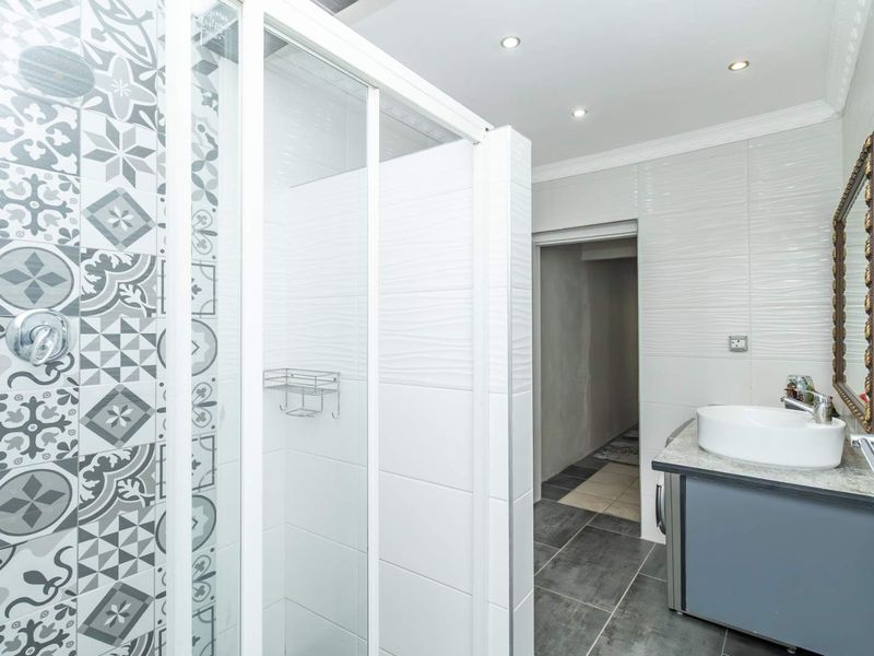 Modern bathroom featuring a glass shower enclosure with decorative patterned tiles, a vanity basin with stone countertop, and recessed ceiling lighting.