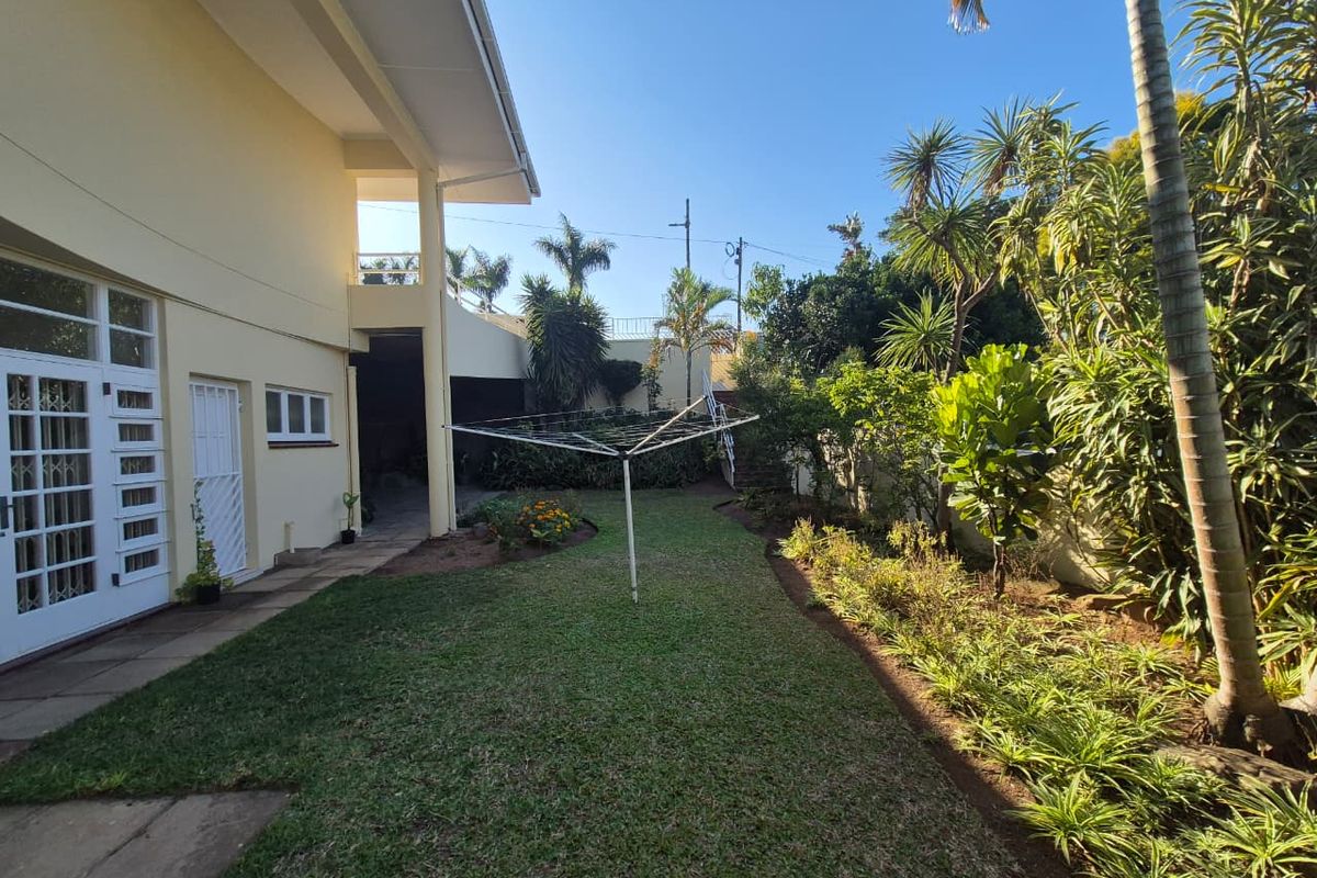 A well-maintained rear garden featuring a lawn, paved patio area, and established perimeter landscaping, accessible via double french doors.