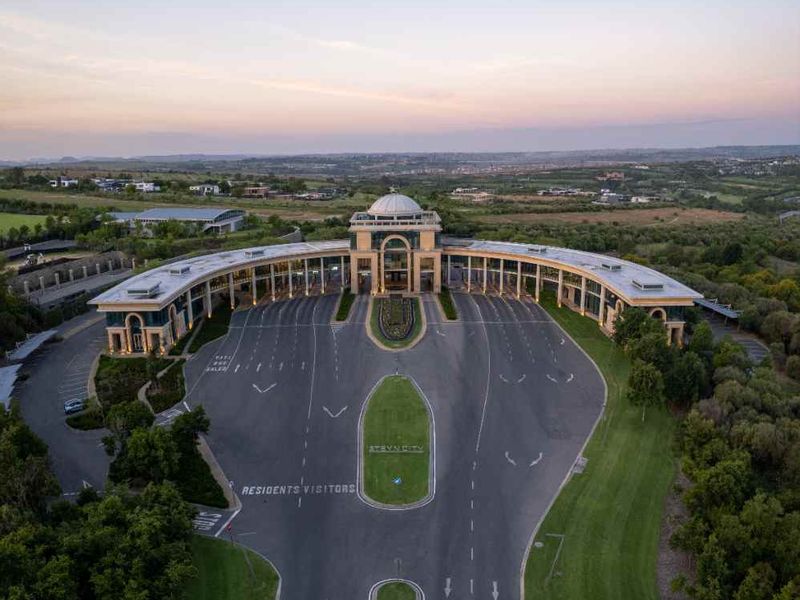 Aerial view of a grand estate entrance featuring a sweeping driveway, landscaped grounds, and a prominent domed architectural structure.
