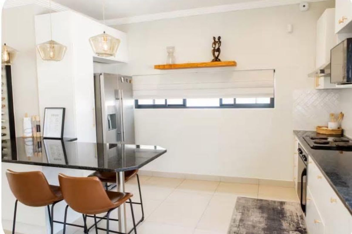 Modern kitchen featuring white cabinetry, dark granite countertops, a breakfast bar, built-in oven, and hob, complemented by tiled flooring and contemporary pendant lighting.
