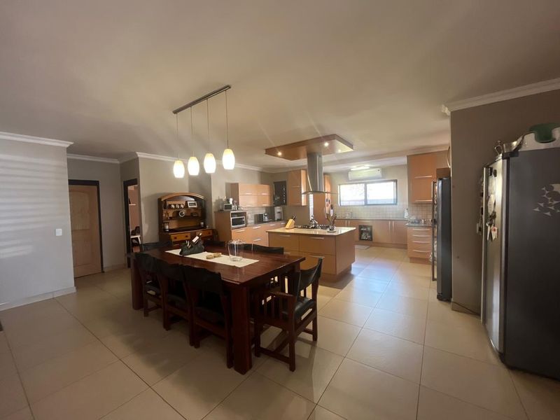 Spacious open-plan kitchen and dining area featuring modern cabinetry, a central island with a built-in cooktop, and neutral tiled flooring throughout.