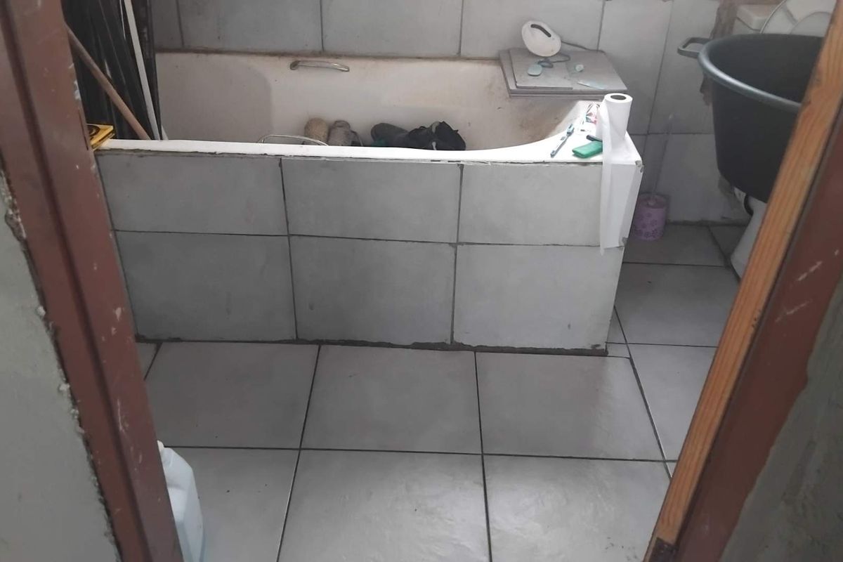 A dated bathroom featuring a tiled bathtub surround and floor tiles, requiring cosmetic updates and maintenance to improve its overall condition.