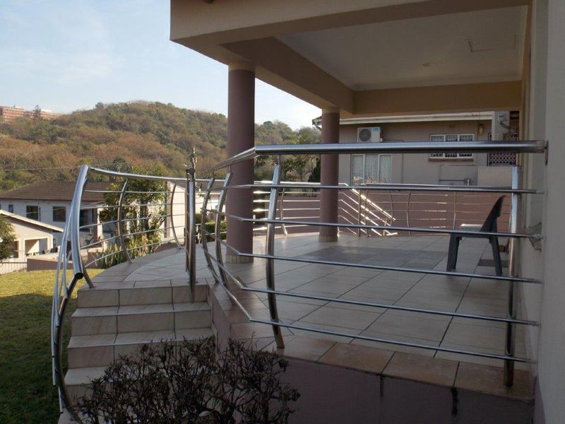 A spacious covered patio featuring tiled flooring and a modern stainless steel balustrade, offering an elevated view of the surrounding landscape.