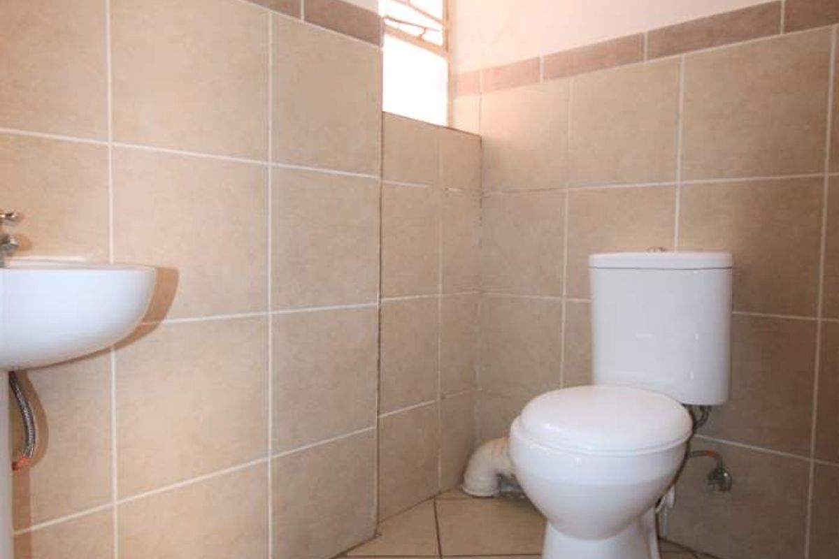 A functional bathroom featuring ceramic wall and floor tiles, a pedestal basin, and a standard toilet.