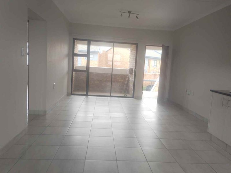 An open-plan living area featuring tiled flooring, neutral walls, and a sliding glass door leading to an outdoor balcony space.