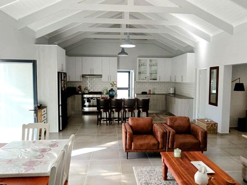 Spacious open-plan living area featuring a modern kitchen with subway tile backsplash, vaulted ceilings with exposed rafters, and large format floor tiles.