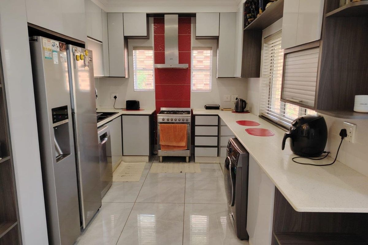 Modern kitchen featuring high-gloss cabinetry, stone countertops, stainless steel gas stove with extractor fan, and polished tiled flooring.