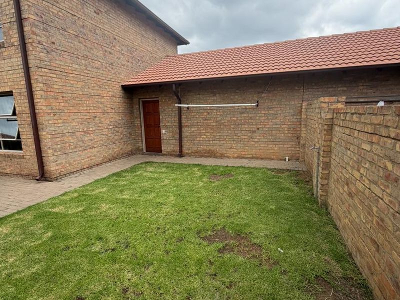 A private rear garden area featuring a paved walkway, established lawn, face brick boundary walls, and a wall-mounted washing line.
