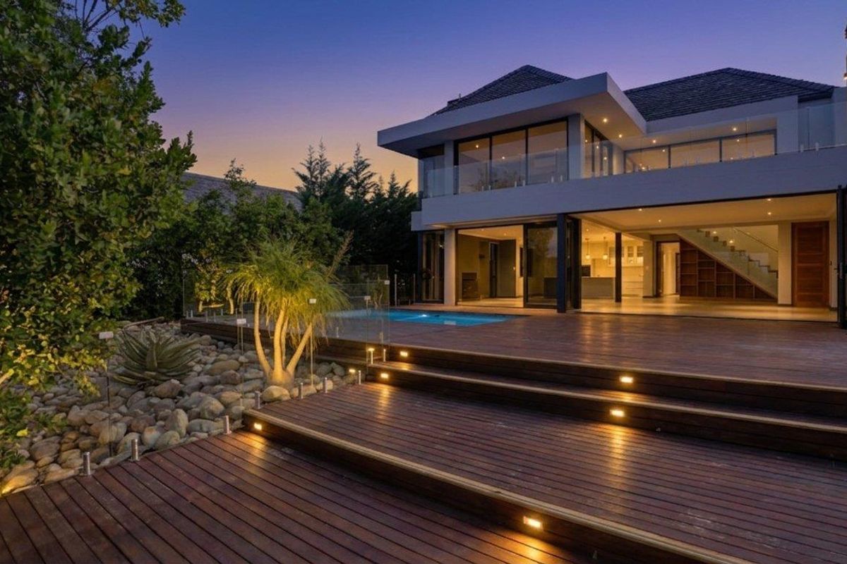 Modern double-story residence featuring a spacious timber deck, integrated swimming pool, glass balustrades, and seamless indoor-outdoor flow through large sliding glass doors.