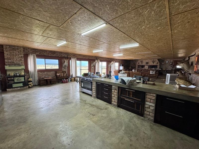 Spacious open-plan living and kitchen area featuring exposed brick walls, concrete floors, and a unique OSB board ceiling with integrated kitchen island.