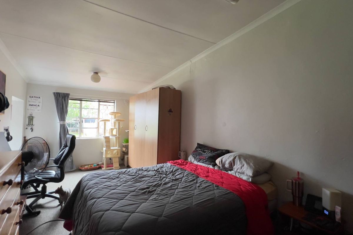 A standard bedroom featuring a window with security bars, neutral wall finishes, and a ceiling-mounted light fixture.