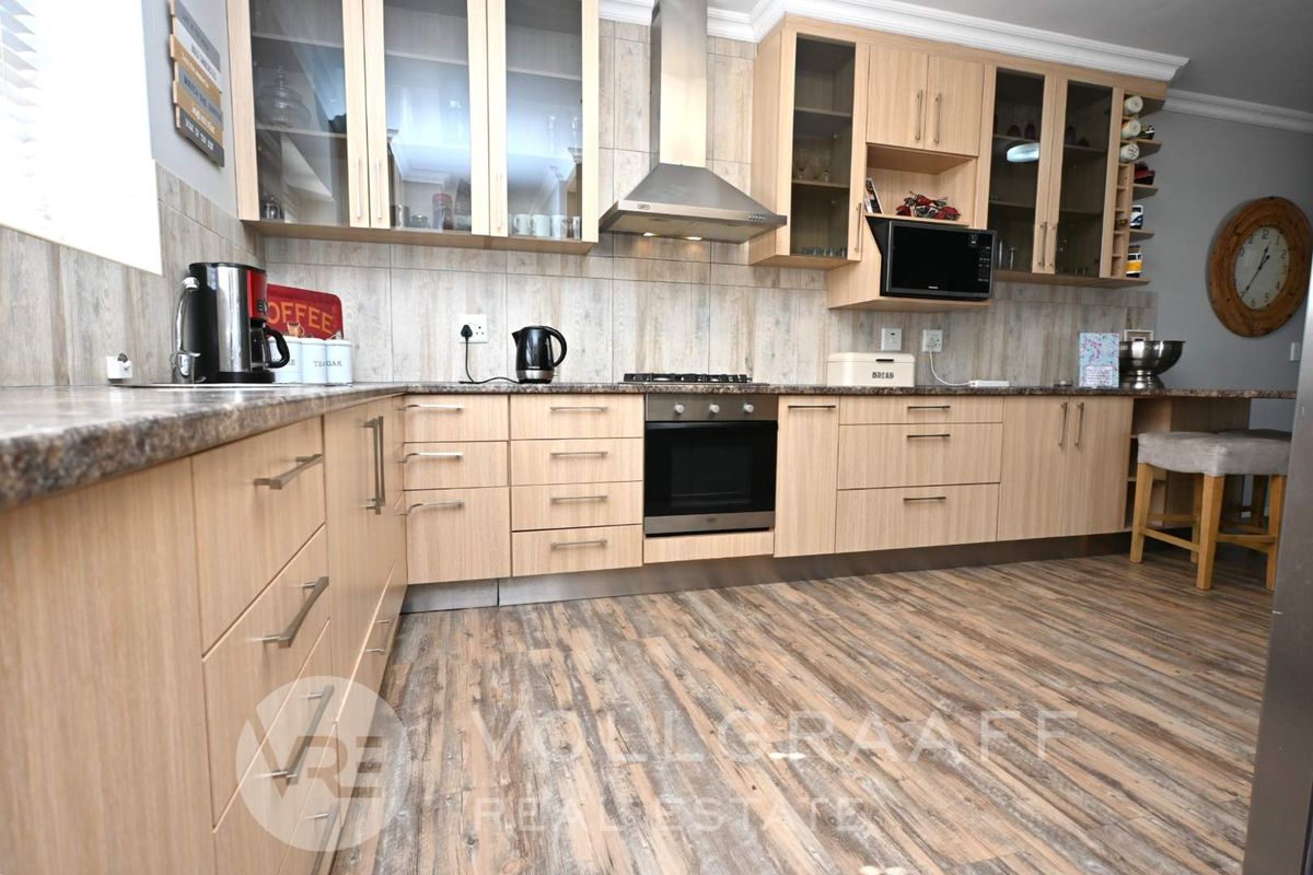 A well-maintained kitchen featuring light wood cabinetry, stone-look countertops, a built-in oven, gas hob, and stainless steel extractor fan.