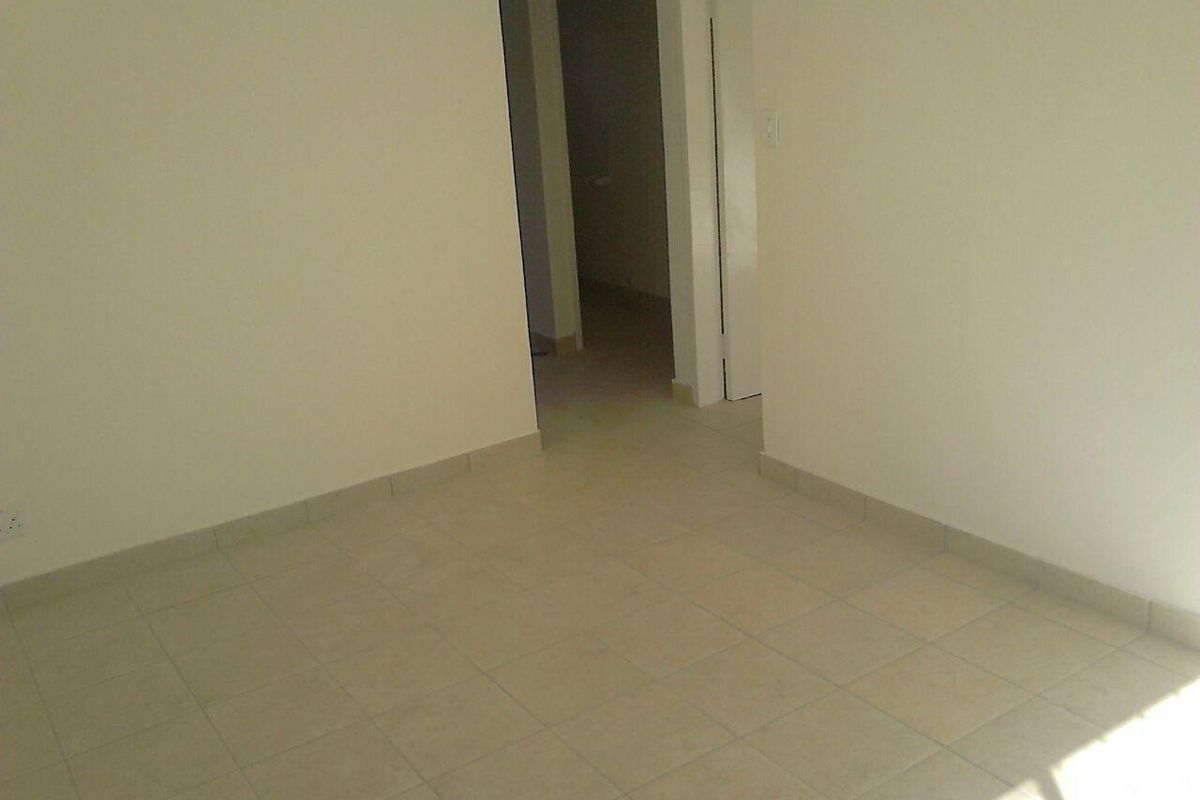 An empty, neutral-toned room featuring tiled flooring and a doorway leading to an adjacent space.