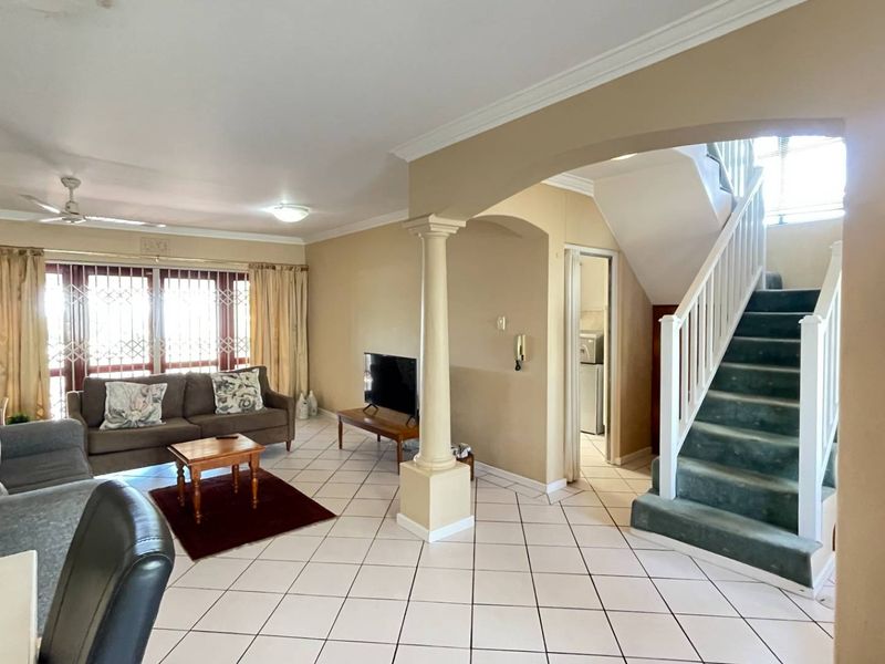 Spacious living area featuring tiled flooring, a decorative column, and a staircase leading to the upper level.