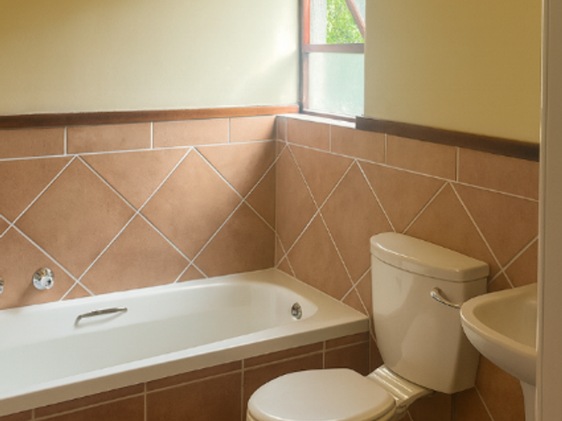 A functional bathroom featuring a bathtub, pedestal basin, and toilet with dated ceramic tiling and natural light from a casement window.