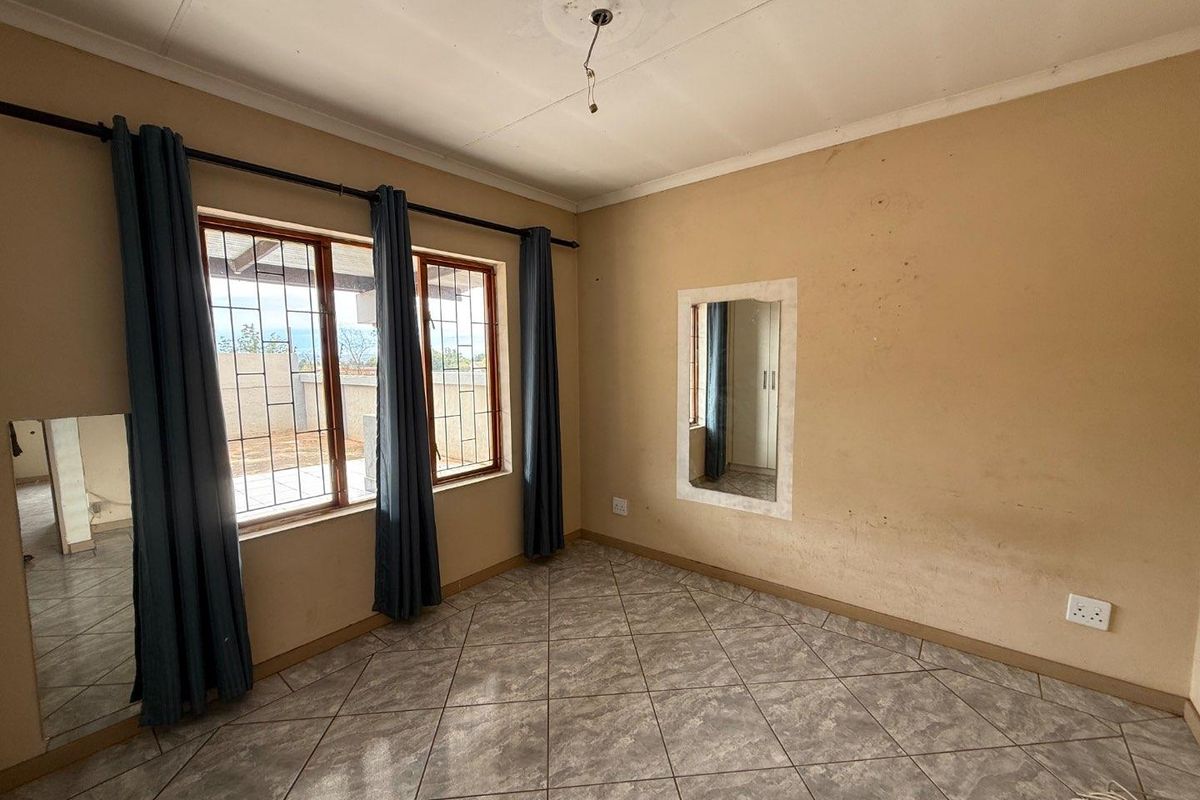 A bedroom featuring tiled flooring, large windows with security bars, and a built-in wall mirror, requiring cosmetic updates to the walls and lighting.