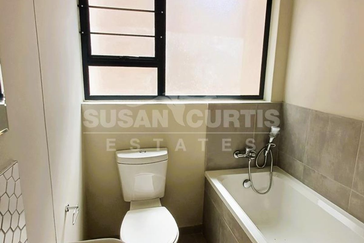 A clean, modern bathroom featuring a white bathtub with a handheld shower mixer, a pedestal basin, and a toilet, finished with neutral wall tiling.