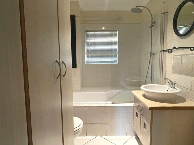 A functional bathroom featuring a shower-over-bath combination, a vessel sink vanity, and built-in storage cabinetry with neutral wall and floor tiling.