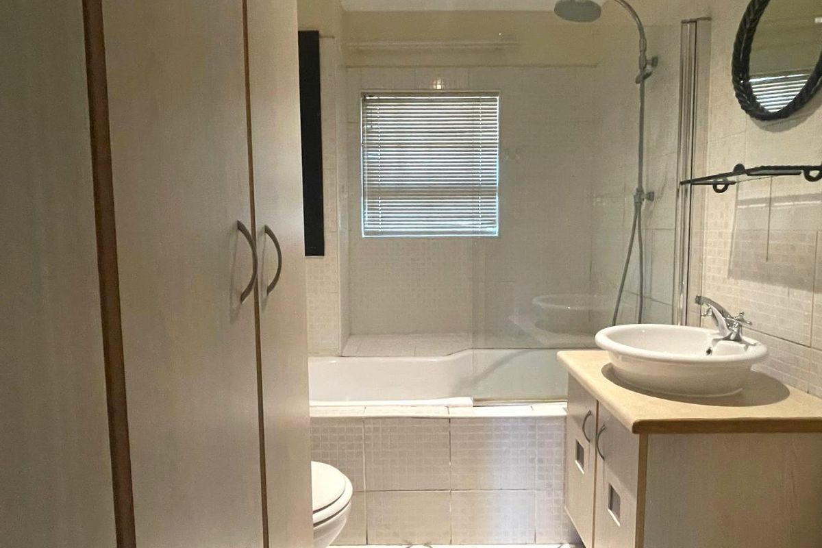 A functional bathroom featuring a shower-over-bath combination, a vessel sink vanity, and built-in storage cabinetry with neutral wall and floor tiling.