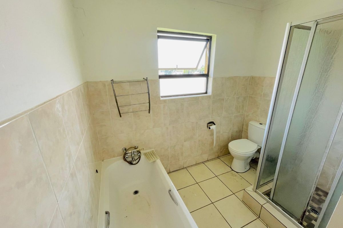 A functional bathroom featuring a bathtub, separate shower enclosure, toilet, and tiled finishes, offering a practical layout for an apartment.