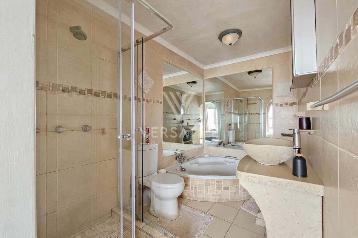 A bathroom featuring a glass-enclosed shower, a corner soaking tub, and a stone-style pedestal basin with large wall-mounted mirrors.