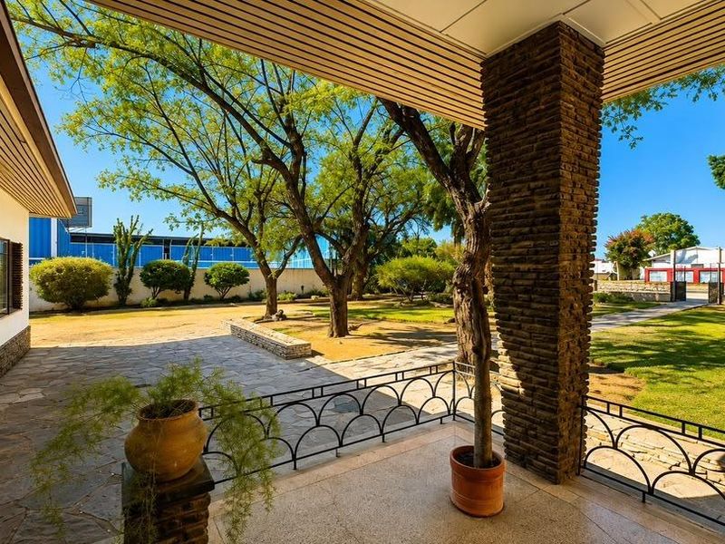 A spacious covered patio featuring stone flooring, a decorative stone-clad pillar, and metal railings, overlooking a well-maintained garden area.