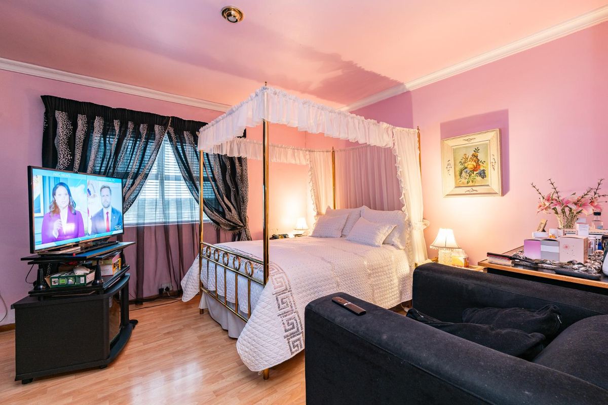 A bedroom featuring laminate flooring and crown molding, currently styled with a canopy bed and pink wall finishes.