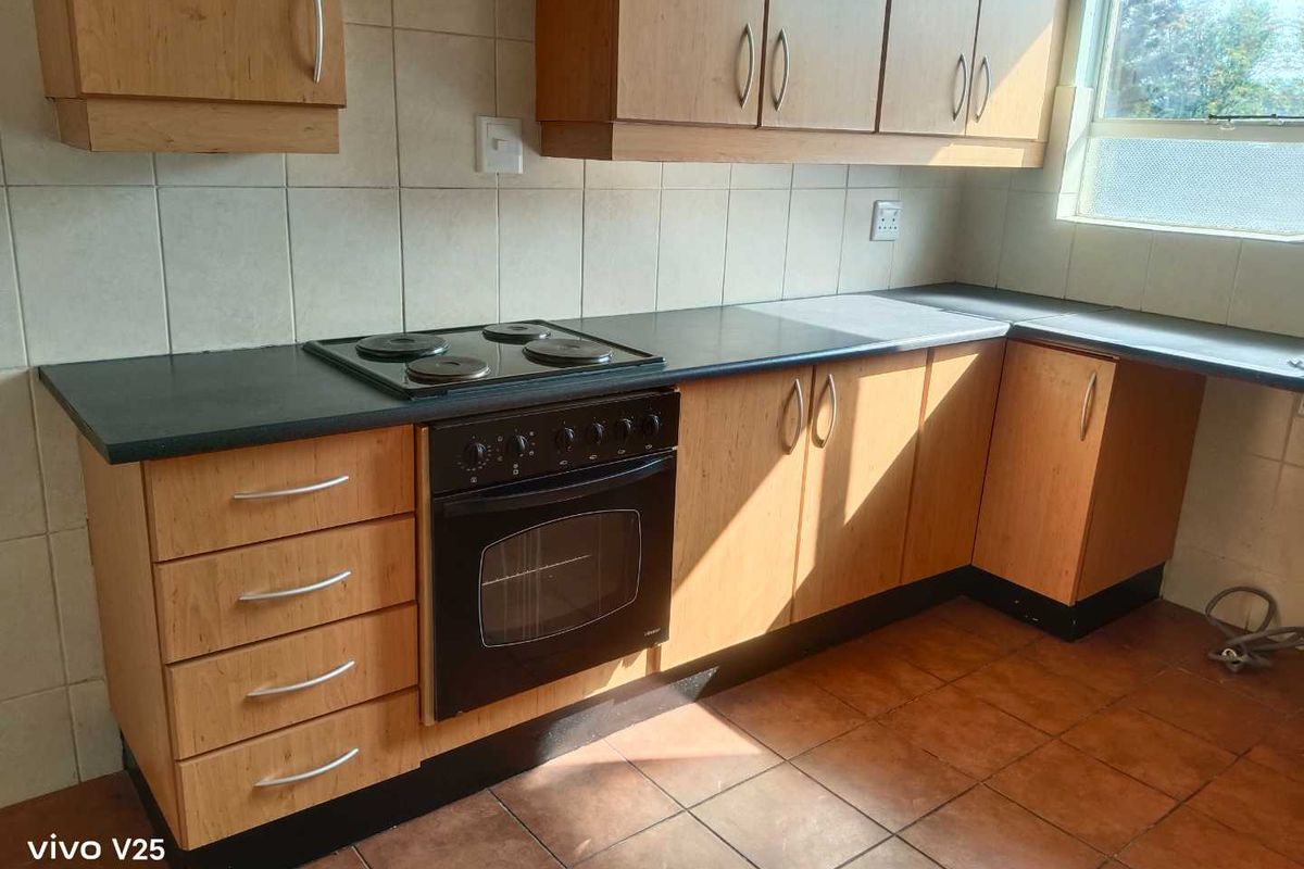 A functional kitchen featuring wooden cabinetry, a built-in oven and hob, tiled backsplash, and tiled flooring, offering a practical layout for daily use.