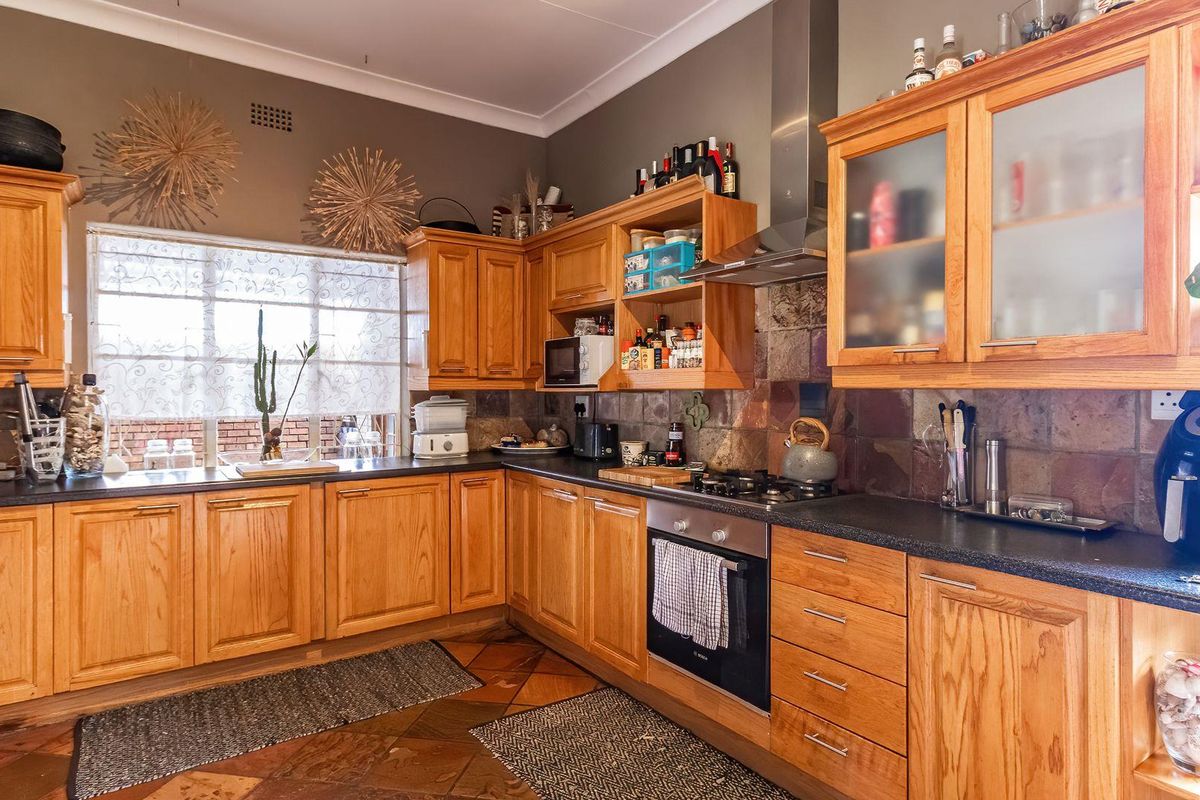 A functional kitchen featuring wooden cabinetry, stone-style tile backsplash, built-in oven, gas hob, and stainless steel extractor fan.