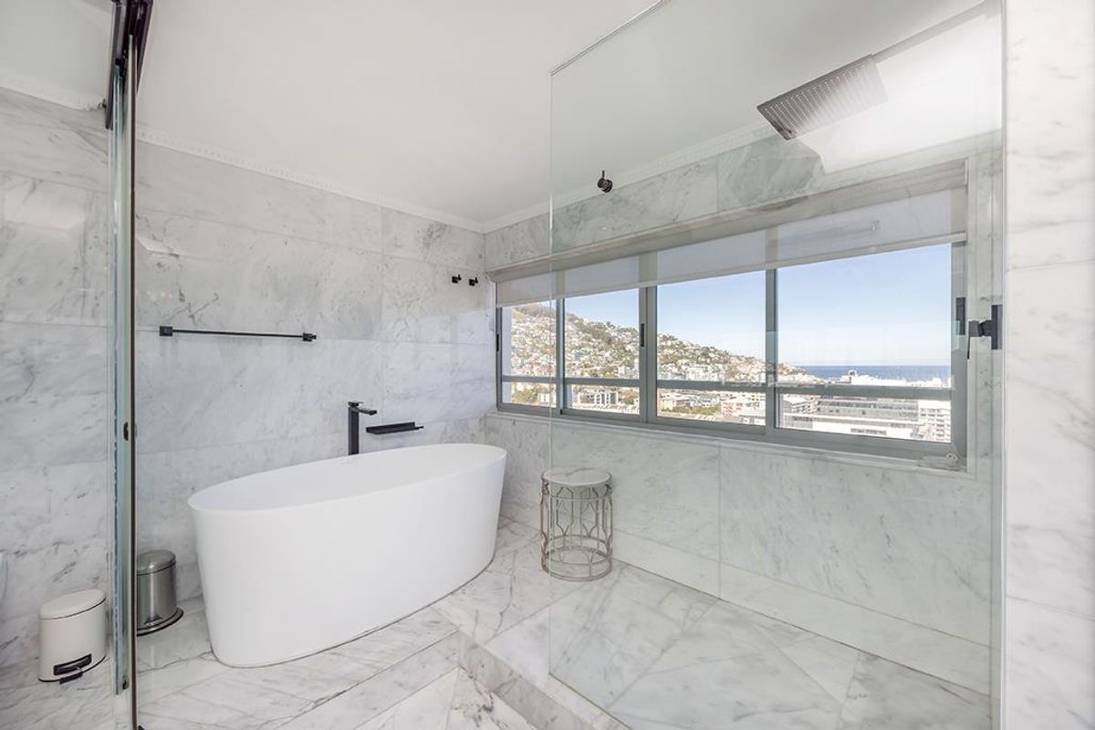 Modern luxury bathroom featuring marble wall and floor tiles, a sleek freestanding bathtub, and a spacious walk-in shower with black matte fixtures.