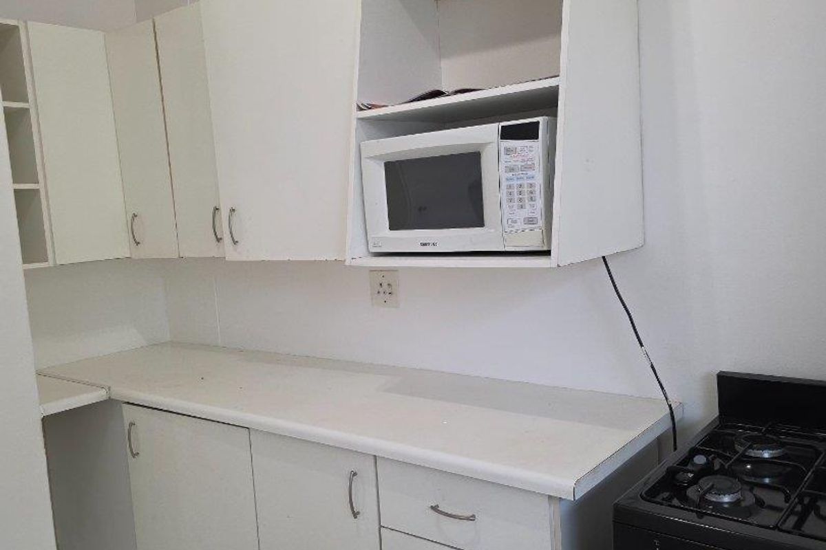 A functional kitchen area featuring white built-in cabinetry, laminate countertops, and a freestanding stove with tiled flooring.