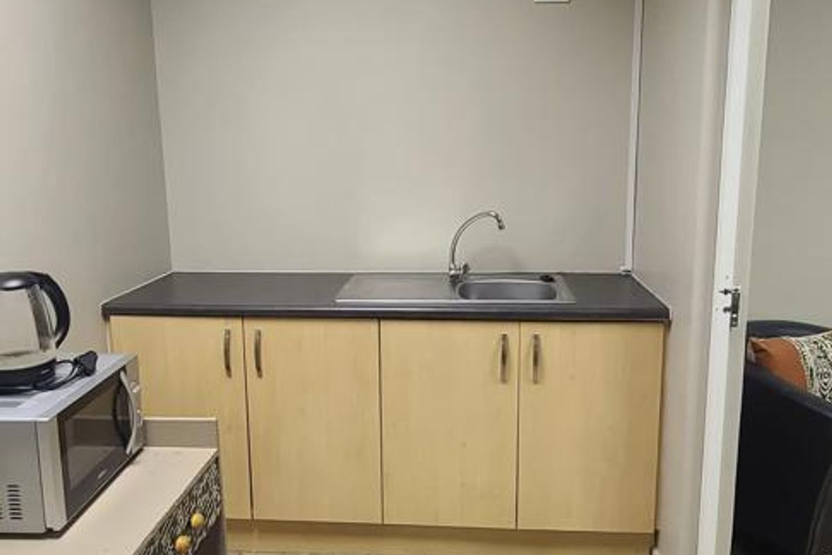 A functional office kitchenette featuring light wood cabinetry, a stainless steel sink, and a drop ceiling with integrated lighting.