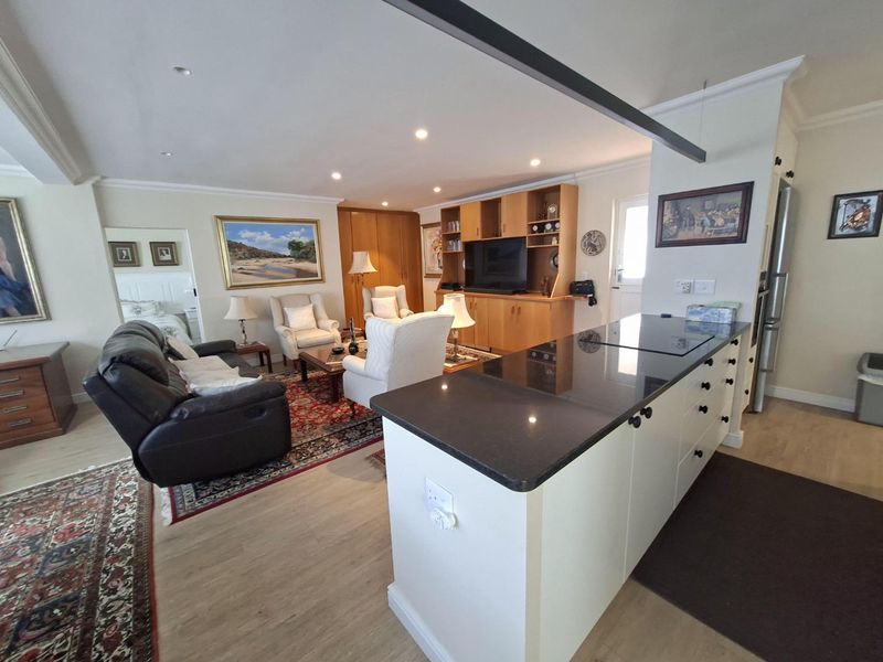 Spacious open-plan living area featuring a modern kitchen island with stone countertops, integrated cabinetry, and light-toned laminate flooring throughout.
