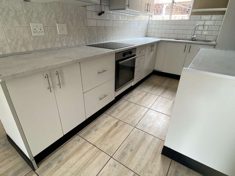 A functional kitchen featuring white cabinetry, subway tile backsplash, built-in oven and hob, and neutral ceramic floor tiles.