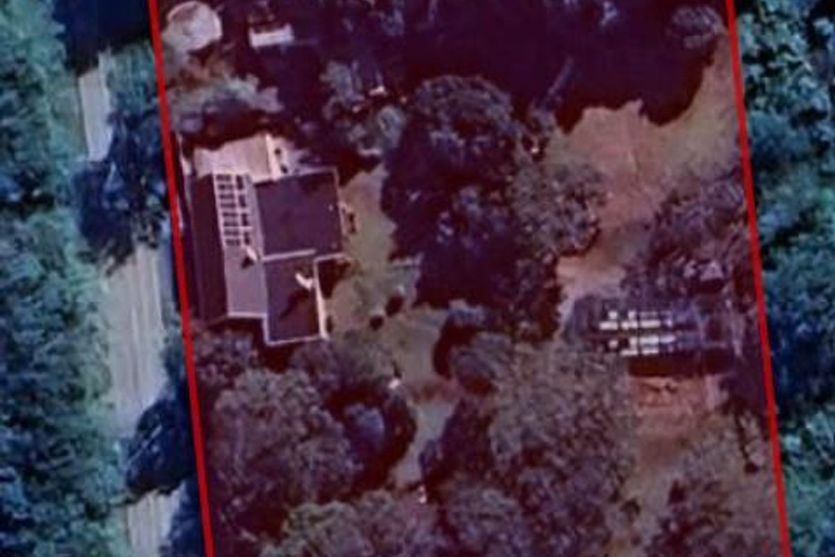 An aerial view of the lodge property, showcasing the building layout, surrounding grounds, and mature tree canopy within the defined boundary.