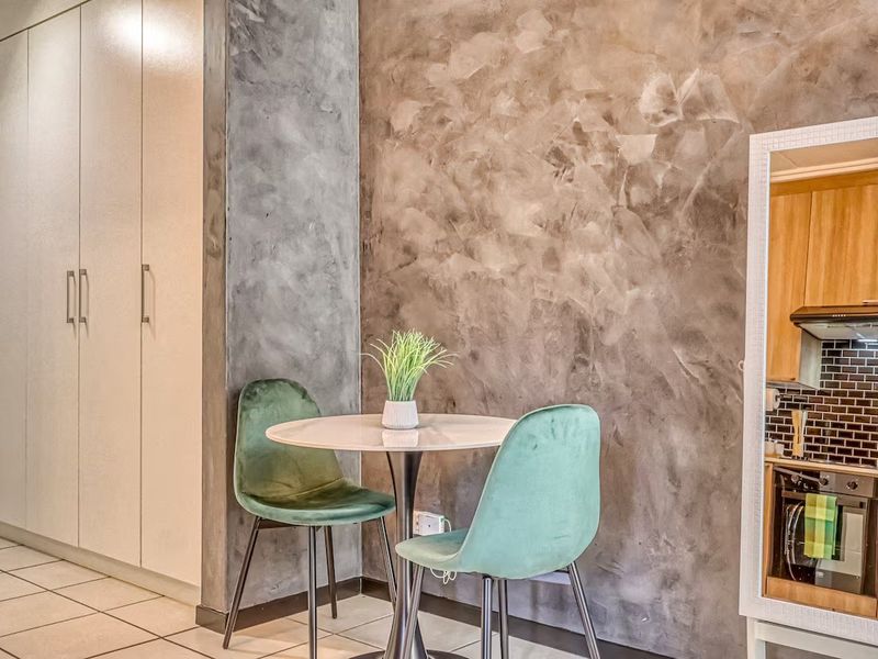 Open plan living area featuring a textured feature wall, tiled flooring, and built-in cupboards, with a glimpse into the modern kitchen.