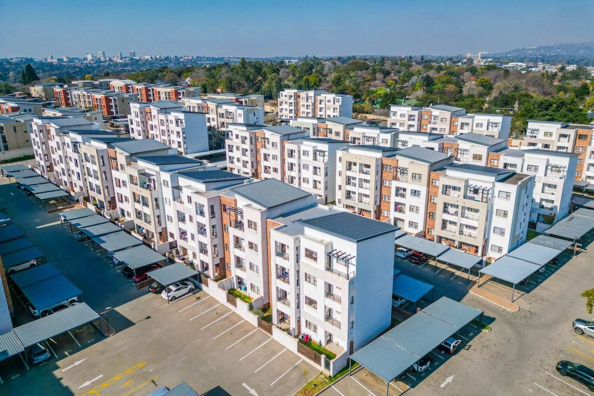 Aerial view of a modern apartment complex featuring multi-story residential buildings, paved parking areas, and covered carports.